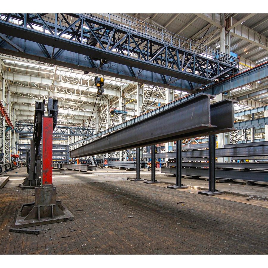 Overhead gantry crane lifting steel H beams in workshop